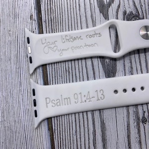 May include: Two white Apple Watch bands with engraved text. The top band reads "Your lifetime roots are your people" with a heart symbol. The bottom band reads "Psalm 91:4-13".