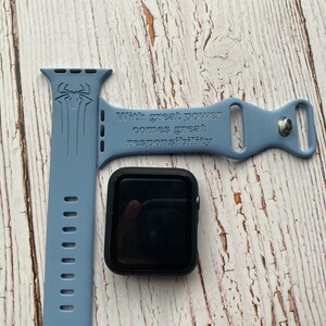 May include: A light blue silicone Apple Watch band with a black Spiderman graphic and the text "With great power comes great responsibility".