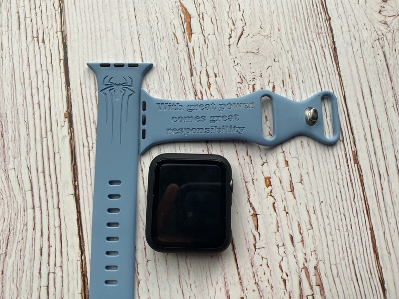 May include: A light blue silicone Apple Watch band with a black Spiderman graphic and the text "With great power comes great responsibility".
