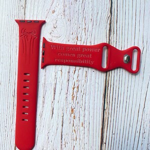 May include: Red silicone Apple Watch band with a Spiderman logo and the quote "With great power comes great responsibility".