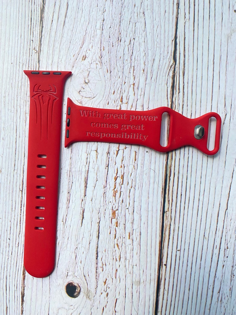 May include: Red silicone Apple Watch band with a Spiderman logo and the quote "With great power comes great responsibility".
