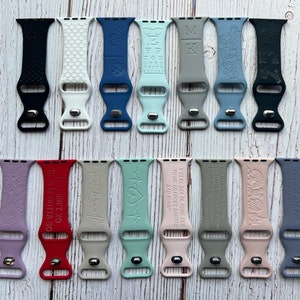 May include: A collection of 20 different coloured silicone watch bands with various engraved designs and text. The bands are all the same size and style, with a buckle closure. Some of the designs include a butterfly, a heart, a cross, and a quote.