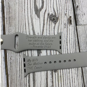 May include: Gray Apple Watch band with engraved text: "Strength and dignity are her clothing, and she smiles at the future. - Proverbs 31:25" and "My Wife Our Mother THE Coach".