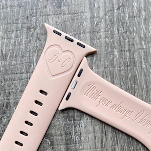 May include: A pink silicone Apple Watch band with a heart engraved with the initials "B+C" and the text "With you always, I love you".