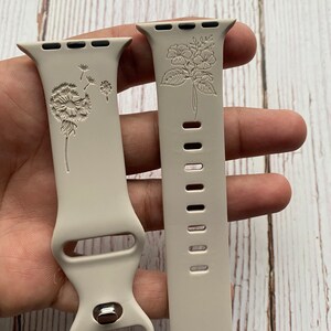 May include: Two beige silicone Apple Watch bands with floral designs. One band features a dandelion design, and the other features a cluster of flowers.