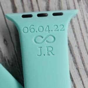 May include: A light blue Apple Watch band with the date 06.04.22, an infinity symbol, and the initials J.R. engraved on it.