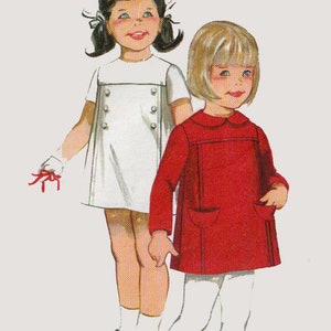 May include: Two girls wearing dresses. The girl on the left is wearing a white dress with buttons and a red bow. The girl on the right is wearing a red dress with a white collar and white tights.