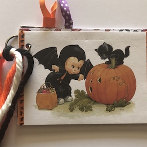 Pode incluir: Um cartão temático de Halloween com uma criança vestida de morcego segurando uma sacola de doces e olhando para uma abóbora talhada com um gato preto no topo.