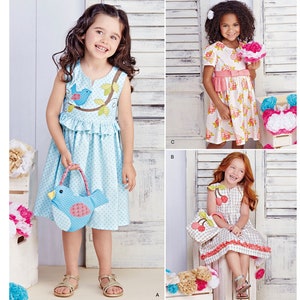 May include: A sewing pattern for girls' dresses with a bird and cherry theme. The pattern includes three different styles: a sleeveless dress with a bird applique, a short-sleeved dress with a floral print, and a sleeveless dress with a gingham pattern. The pattern is designed and printed in the USA.