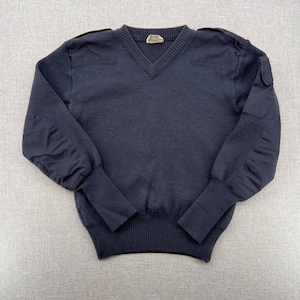 May include: Navy blue V-neck sweater with reinforced shoulder and elbow patches. The sweater has ribbed cuffs and a ribbed hem. The patches are a darker shade of navy blue. The sweater has a small tag at the neckline.