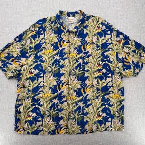 May include: A short-sleeved button-down shirt featuring a vibrant pattern of Mickey Mouse, bananas, and tropical foliage. The shirt's design incorporates a blue background with tan and green accents, creating a playful and colorful aesthetic. The shirt has a classic collar.