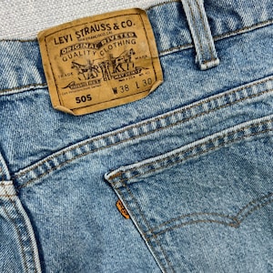 May include: Close-up of light blue denim jeans with a brown leather Levi Strauss & Co. label. The label reads "ORIGINAL RIVETED CLOTHING" and "W 38 L 30". The jeans have a classic five-pocket design.