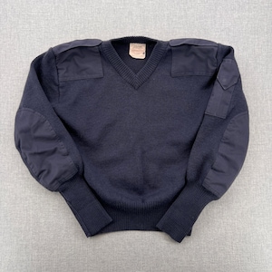 May include: Navy blue V-neck sweater with reinforced patches on the shoulders and elbows. The sweater has ribbed cuffs and a ribbed hem. A small tag is sewn into the neckline. The sweater is made of a thick knit material.