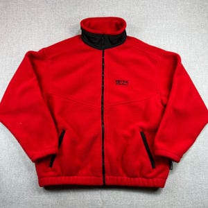 May include: A red fleece jacket with a black collar and a full-length zipper. The jacket has two side pockets and the text "EBTEK" on the chest. The jacket is a medium size.