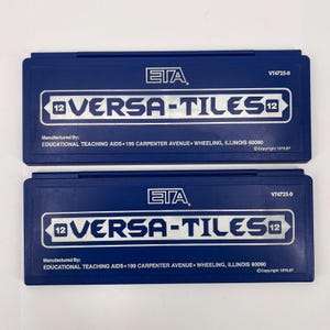 May include: Two blue VERSA-TILES 12 cases are displayed. Each case has the ETA logo and the text "VERSA-TILES 12" in a white rectangle. The text "Manufactured By: EDUCATIONAL TEACHING AIDS" is also visible.