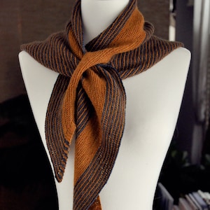 May include: A brown and navy blue striped knitted scarf with a fringed edge. The scarf is draped over a white mannequin.