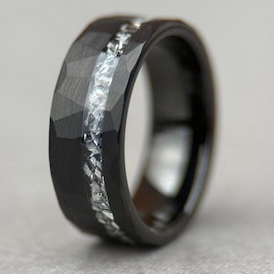 May include: A black ring with a faceted surface and a silver inlay. The ring has a modern design and a polished finish. The silver inlay runs down the center of the ring.