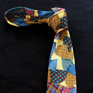 May include: A yellow, blue, red, and green patterned silk tie. The tie has a geometric pattern with a variety of shapes and sizes.