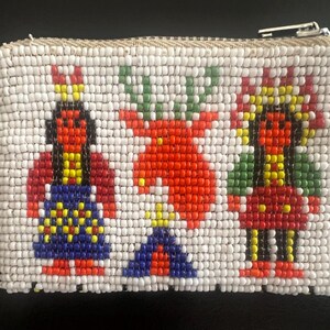 May include: White beaded coin purse with a zipper closure. The purse features a colorful beaded design of three figures in red, blue, yellow, and green. The figures appear to be Native American inspired.