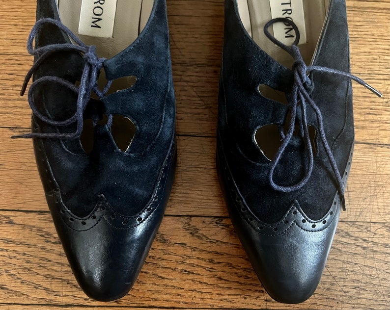 Puede incluir: Un par de zapatos de ante azul marino con cierre de cordones y un dise&ntilde;o decorativo de corte. Los zapatos tienen una punta puntiaguda y una suela de cuero. El nombre de la marca "TROM" es visible en el interior de los zapatos.