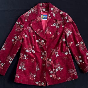 May include: Burgundy floral blazer with a single-button closure and two front pockets. The blazer has a repeating pattern of white, pink, and brown flowers. The label reads "King's".