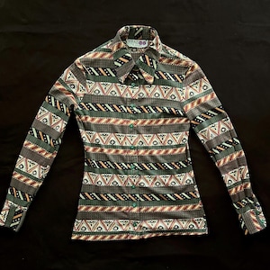 Könnte beinhalten: Langärmliges Hemd mit geometrischem Muster in Grau-, Grün- und Brauntönen. Das Hemd hat einen Kragen, geknöpfte Manschetten und grüne Knöpfe. Der Markenname "JIKADOO" ist auf dem Kragen sichtbar.