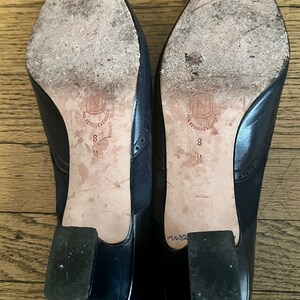 Puede incluir: Un par de zapatos de tac&oacute;n de cuero azul marino con un tac&oacute;n de cuero negro. Los zapatos tienen una suela de cuero blanco con el texto "All Genuine Leather" y "8 M" impreso en la suela.