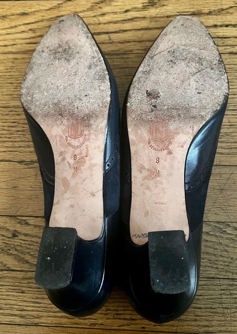 Puede incluir: Un par de zapatos de tac&oacute;n de cuero azul marino con un tac&oacute;n de cuero negro. Los zapatos tienen una suela de cuero blanco con el texto "All Genuine Leather" y "8 M" impreso en la suela.