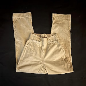 May include: Tan-colored pants with a high waist and wide legs. The pants have a button and zipper closure, along with two front pockets. The fabric appears to be a soft, corduroy-like material.