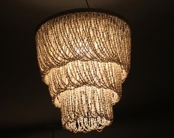 May include: A white beaded chandelier with three tiers of cascading beads. The chandelier is lit and casts a warm glow.