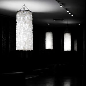 May include: A black and white image of a dimly lit room with three cylindrical pendant lights. The lights are covered in white, circular embellishments, creating a textured, glowing effect. The room's dark ambiance highlights the bright, decorative lights.