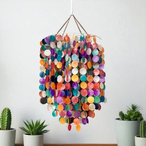 May include: A decorative chandelier made from iridescent shell discs in a variety of colours, including orange, purple, green, and white. The chandelier hangs from a white cord and has a metal frame. The shell discs are arranged in vertical strands.