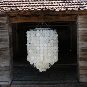 Puede incluir: Una lámpara de araña de conchas blancas con un diseño circular cuelga del techo de un granero rústico.
