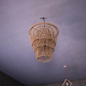 May include: A woven, beige, pendant light fixture hangs from the ceiling. The light fixture is made of multiple layers of woven strands, creating a cascading effect.