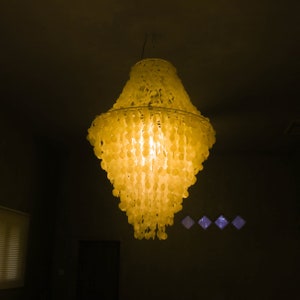 May include: A yellow chandelier made of many small, round, translucent pieces. The chandelier is hanging from the ceiling and is lit, casting a warm glow.