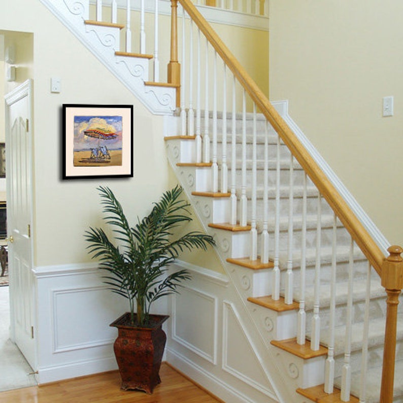 May include: A framed painting of a beach scene with a colorful umbrella and two chairs. The painting is hanging on a white wall in a hallway with a wooden staircase.