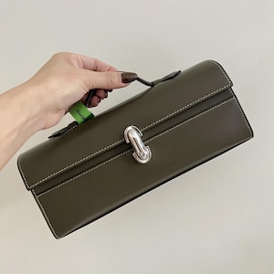 May include: A dark green leather clutch bag with a silver clasp and a top handle. The bag has a subtle stitched design.