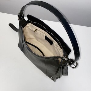 May include: Black leather shoulder bag with a long, curved handle and a smaller strap. The bag is open, revealing a light-colored interior with a zippered pocket. The bag has silver-toned hardware.