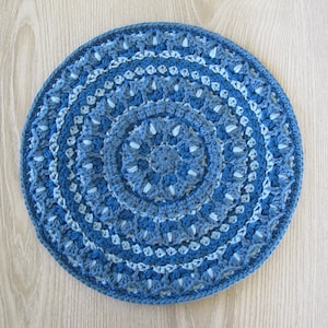 Könnte beinhalten: Ein blaues und graues gehäkeltes Mandala mit einem runden Design. Das Mandala ist aus verschiedenen Blautönen und Grautönen gefertigt.