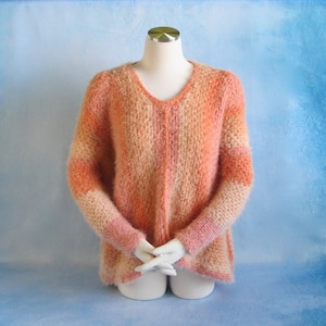 May include: A soft, fuzzy, peach and cream colored sweater with a V-neck and long sleeves.