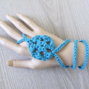 Peut inclure: Un gant sans doigts en crochet bleu turquoise avec un motif floral en crochet décoratif. Le gant est attaché autour du poignet avec un long cordon en crochet.