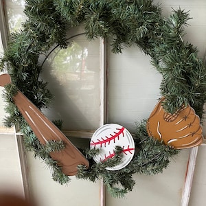 May include: A green wreath with a brown wooden baseball bat, a white baseball with red stitching, and a brown leather baseball glove.