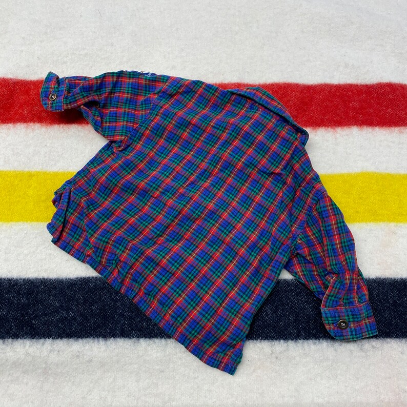 Puede incluir: Una camisa de manga larga a cuadros rojos, azules y verdes con cierre de botones.