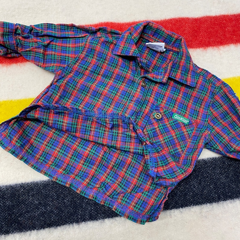 Puede incluir: Una camisa de manga larga a cuadros rojos, azules y verdes con cuello abotonado y un peque&ntilde;o parche verde con el texto "Oak Creek" en el pecho izquierdo.