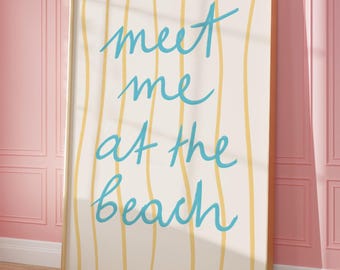 May include: A framed art print with the words "meet me at the beach" in light blue script. The background has vertical yellow stripes on a cream-colored surface. The frame is a light wood color, and the print is leaning against a pink wall.