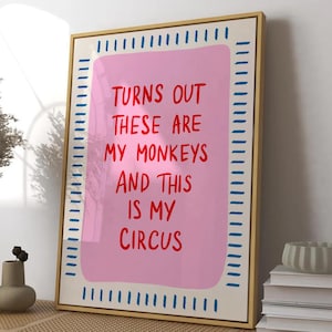 Könnte beinhalten: Gerahmter Kunstdruck mit dem Text "TURNS OUT THESE ARE MY MONKEYS AND THIS IS MY CIRCUS" in Rot auf rosa Hintergrund. Der Rahmen ist goldfarben mit blauen und weißen Akzenten. Die Kunst wird auf einer Holzbank ausgestellt.