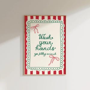 May include: A framed art print with a red and white striped border and a scalloped green edge. The text "Wash your hands ya filthy animal" is written in green script, with red bow accents.