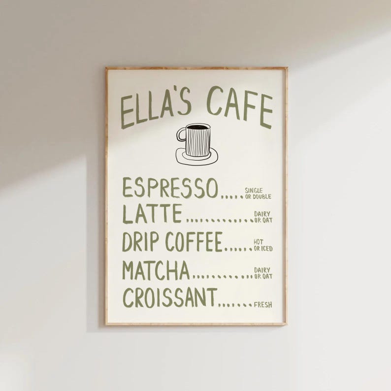 Puede incluir: Un cartel enmarcado con el texto "ELLA'S CAFE" en verde, que enumera opciones de caf&eacute; y pasteler&iacute;a. El men&uacute; incluye espresso, latte, caf&eacute; de goteo, matcha y croissant. Hay una peque&ntilde;a ilustraci&oacute;n de una taza de caf&eacute;.