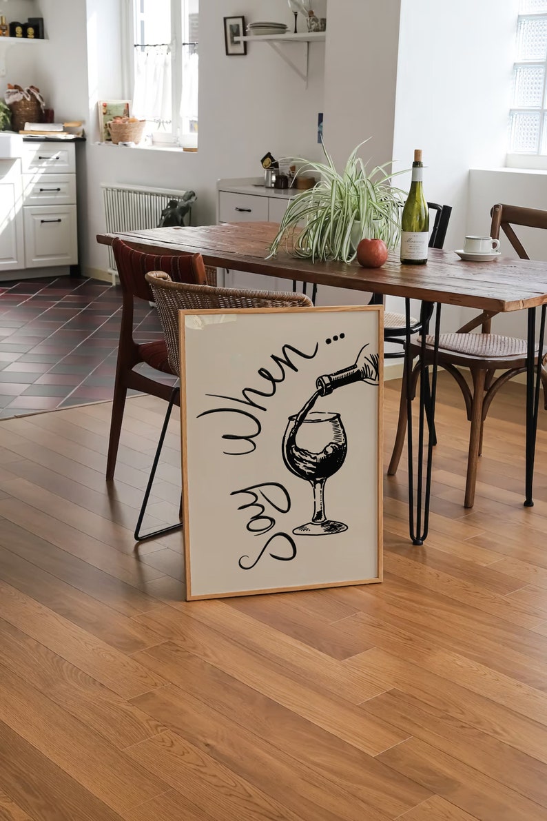 K&ouml;nnte beinhalten: Ein gerahmter Druck mit einer Schwarzwei&szlig;illustration eines Weinglases, in das eine Flasche Wein gef&uuml;llt wird. Der Text "Say When..." ist in einer kursivschriftlichen Schriftart &uuml;ber dem Glas geschrieben.