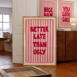 Könnte beinhalten: Drei gerahmte Kunstdrucke mit rosa-weiß gestreiften Hintergründen. Der größte Druck lautet "BETTER LATE THAN UGLY" in roten Buchstaben. Zwei kleinere Drucke sagen "NICE RUM" und "YOU LOOK GOOD".